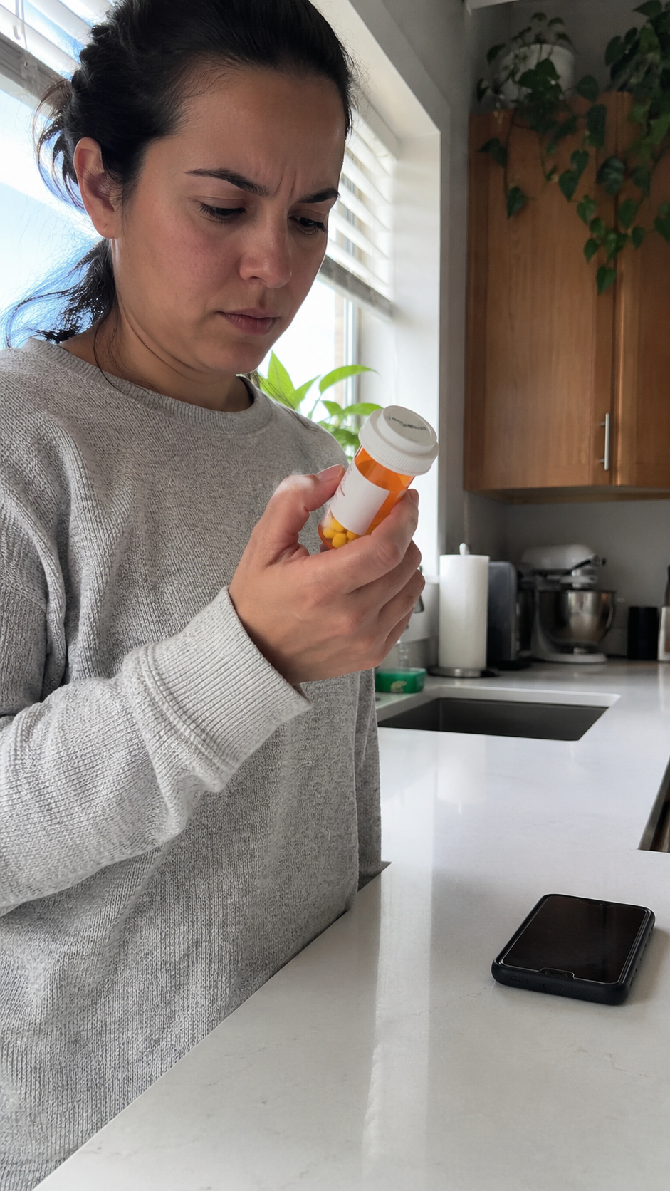 Person reading a medication bottle label with a phone nearby